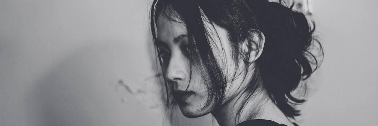 6 Ways to Deal With Suicidal Thoughts, According to Experts Young woman with dark hair pulled back in a money tail rests her head against a white wall