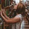 photo of young woman in college library or bookstore, looking at a high shelf of books