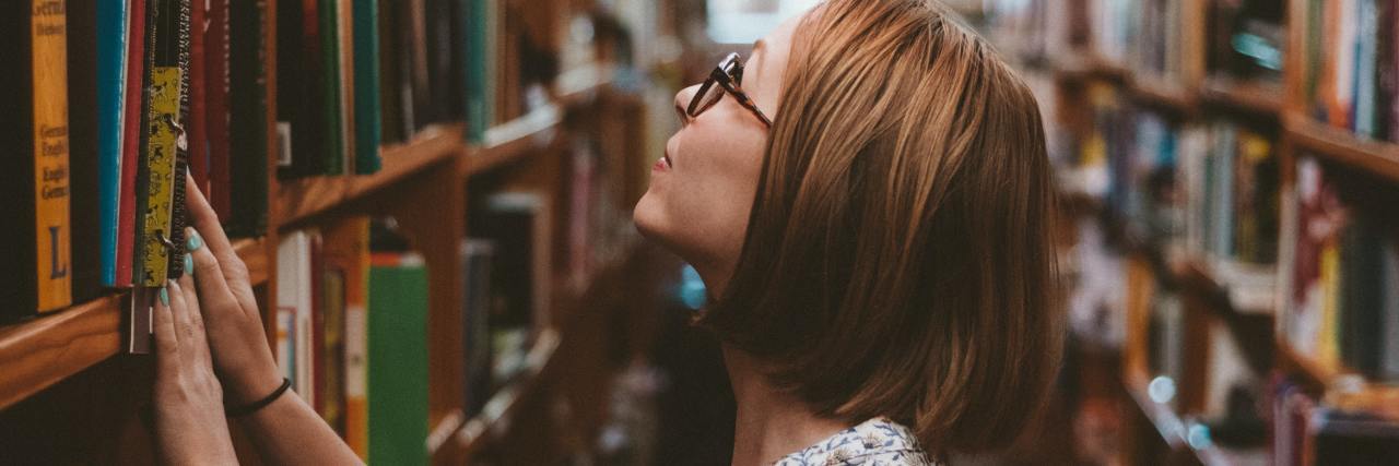College Taught Me To Get Help for My Bipolar Disorder photo of young woman in college library or bookstore, looking at a high shelf of books
