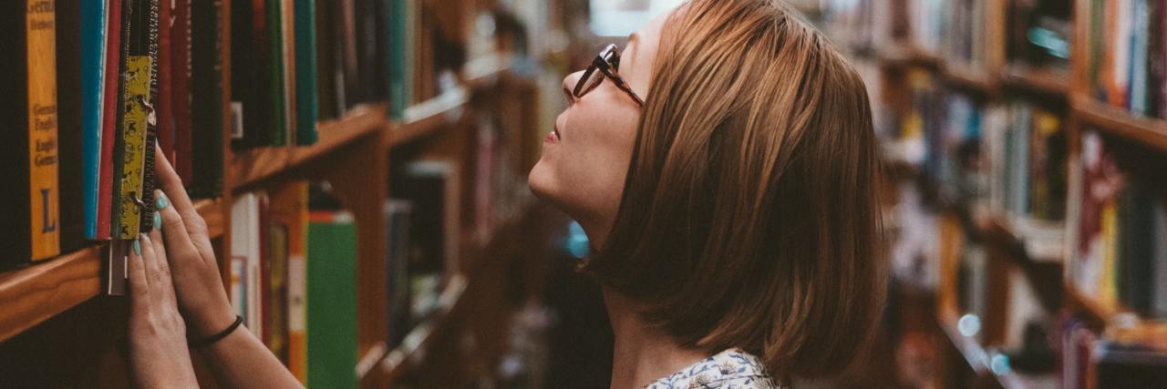 photo of young woman in college library or bookstore, looking at a high shelf of books