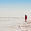 Young girl standing on beach alone looking out over water