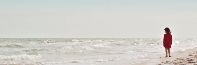 Young girl standing on beach alone looking out over water