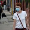 photo of woman standing in street wearing a white shirt and a blue coronavirus face mask