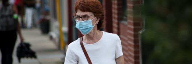 photo of woman standing in street wearing a white shirt and a blue coronavirus face mask