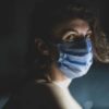 photo of woman with scared expression, looking into camera from side view while wearing a face mask