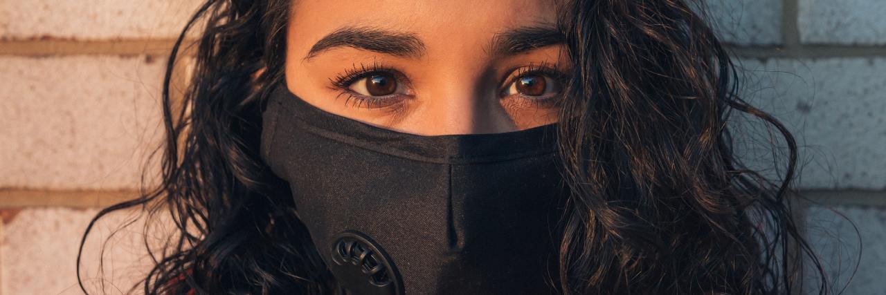 It's Too Soon To End Coronavirus Lockdown photo of black woman wearing a face mask, looking into camera standing against a brick wall