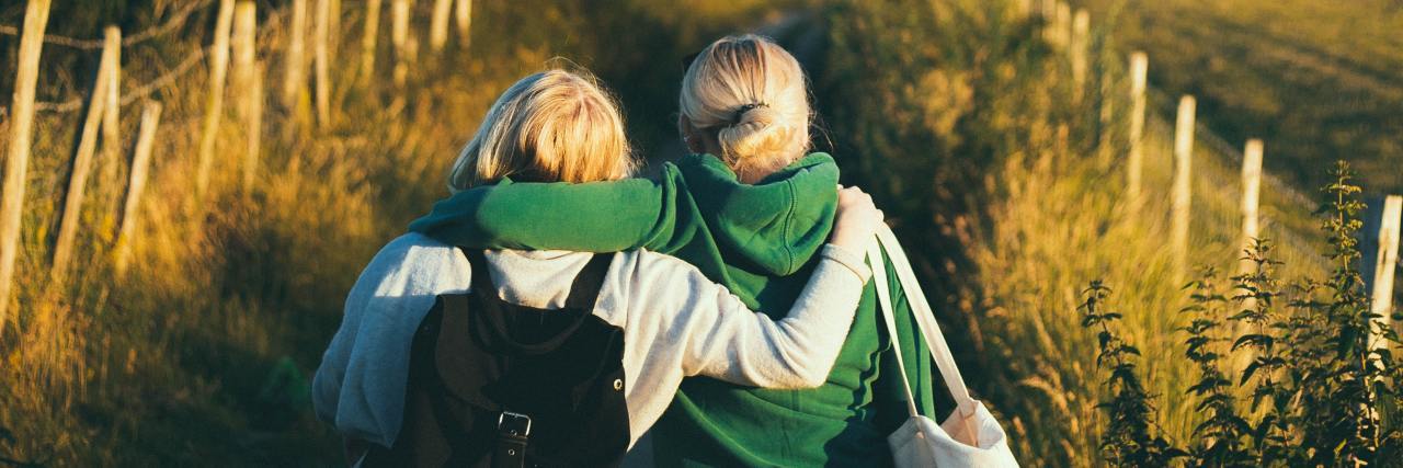 How To Help Someone Get Through a Bad Situation With Anxiety photo of two women walking away from camera down a country lane at sunset, arms around each other's shoulders