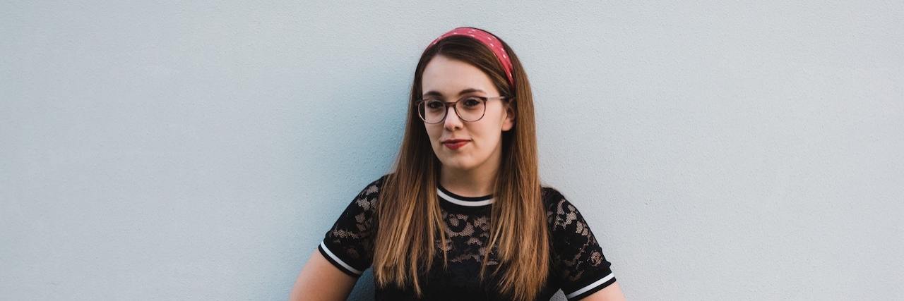 Identifying the Real Reasons Why We Self-Harm Woman wearing glasses standing against a wall