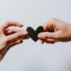 One hand giving a small, black paper heart to another person's hand