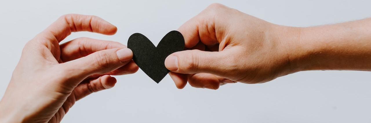 Study: Social Connection Strongest Protection Against Depression One hand giving a small, black paper heart to another person's hand