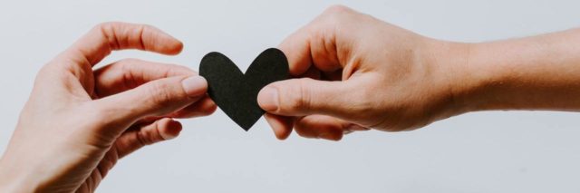 One hand giving a small, black paper heart to another person's hand