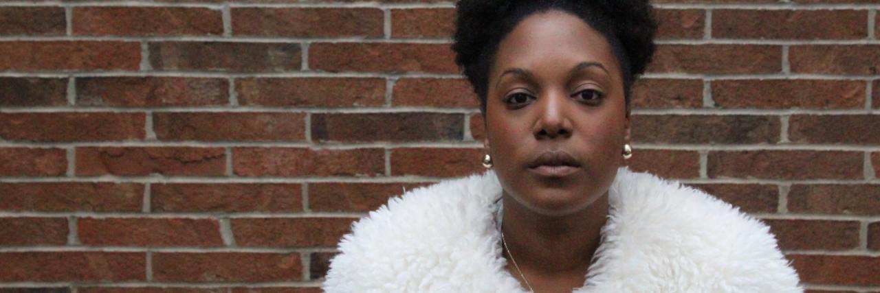 Why Releasing Police Mugshots of Black People Is a Bad Thing photo of woman standing in front of brick wall and looking into camera with serious or sad expression