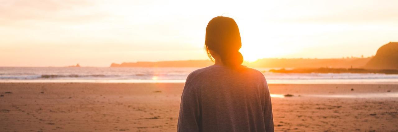 The Difference Between PTSD Flashbacks and Panic Attacks Woman standing on the beach facing the sunset