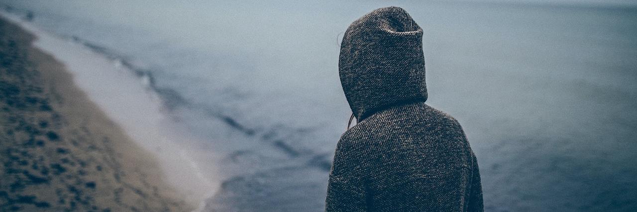 Study Confirms Asking Directly About Suicide Doesn’t Cause More Harm Person wearing a gray hoodie walking along the beach on an overcast day
