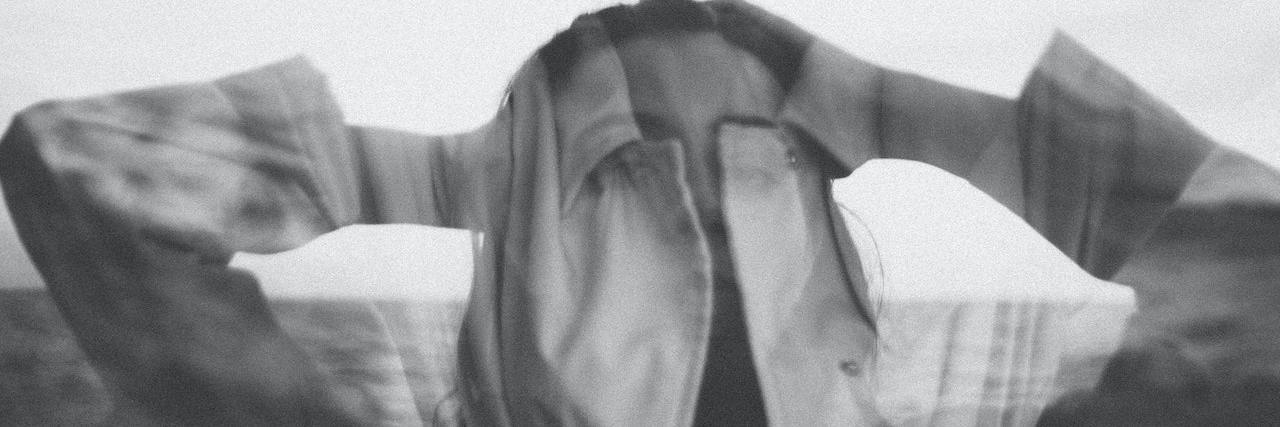 A black and white image of a woman with her hands on her head. Her figure is blurry