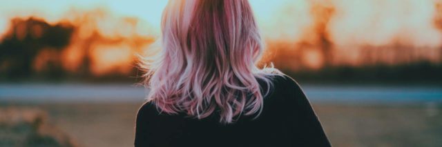 photo of woman with pink hair facing away from camera and looking into distance at sunset