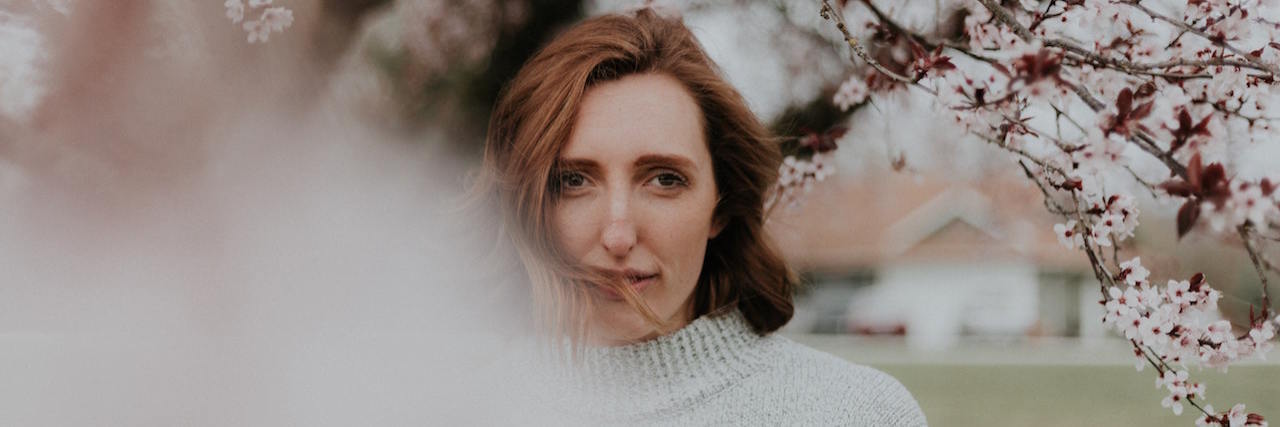 Don't Feel Guilty About Experiencing These 9 Anxiety Symptoms A woman standing in front of a tree with light pink flowers