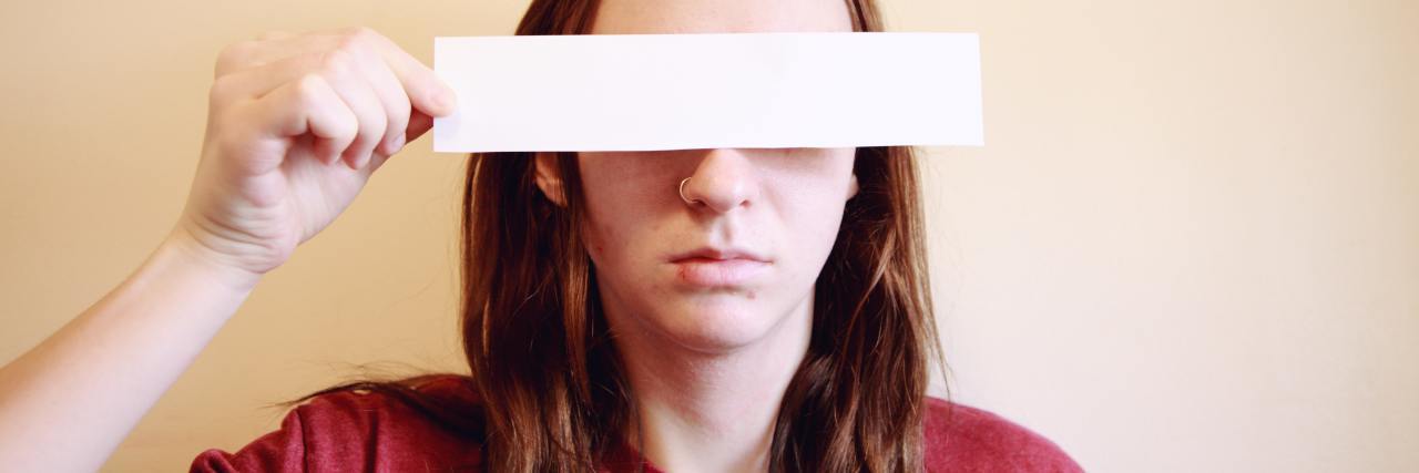 photo of young woman hiding her eyes with a rectangle of paper