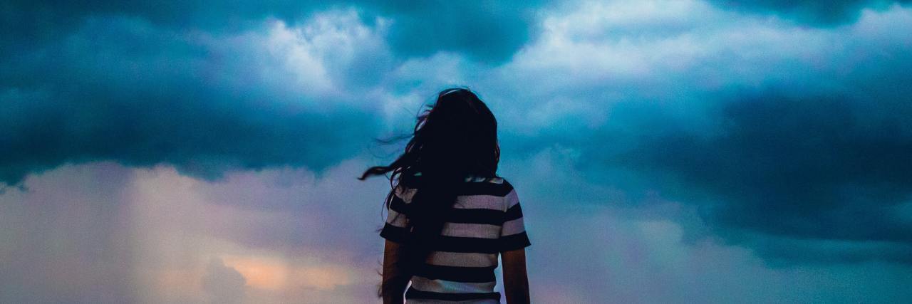 photo of woman facing away from camera, looking at stormy clouds in the distance