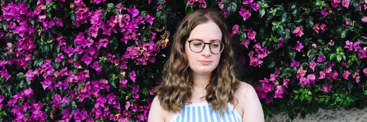 How Going on Autopilot Can Become an Unhealthy Coping Mechanism Woman wearing glasses standing in front of fuchsia flowers