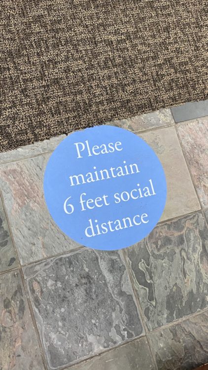A sticker on the ground that reads, "Please maintain 6 feel social distance"