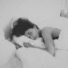 black and white photo of woman lying in bed with sad expression while looking at the camera