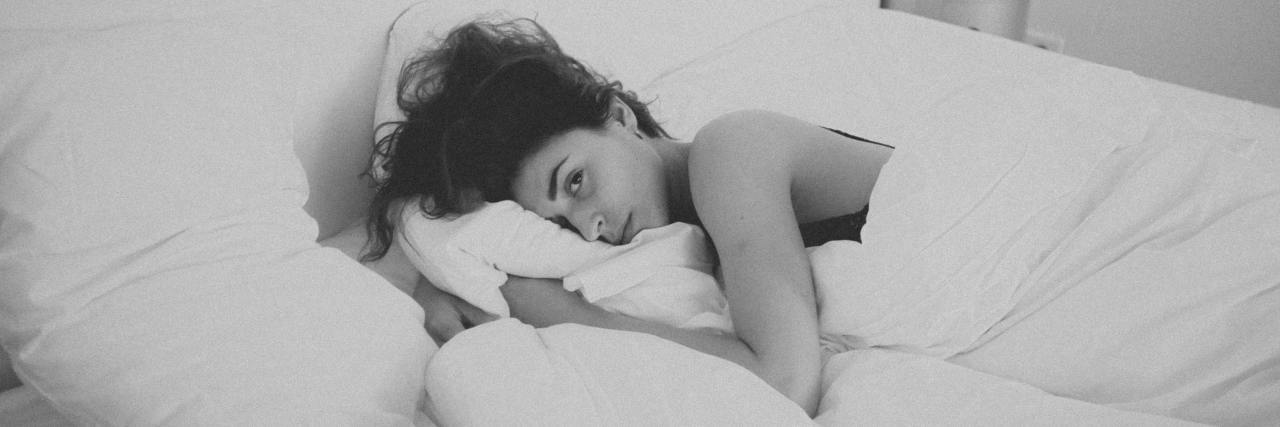 A ‘Typical’ Day With Chronic Suicidal Thoughts black and white photo of woman lying in bed with sad expression while looking at the camera