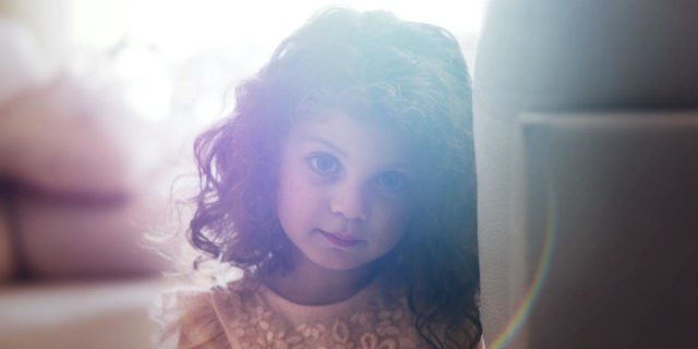 CDC Warns of Higher Potential for Rare Childhood Virus AFM This Year Young girl with curly brown hair wearing an orange top leans against a wall and looks directly at the camera