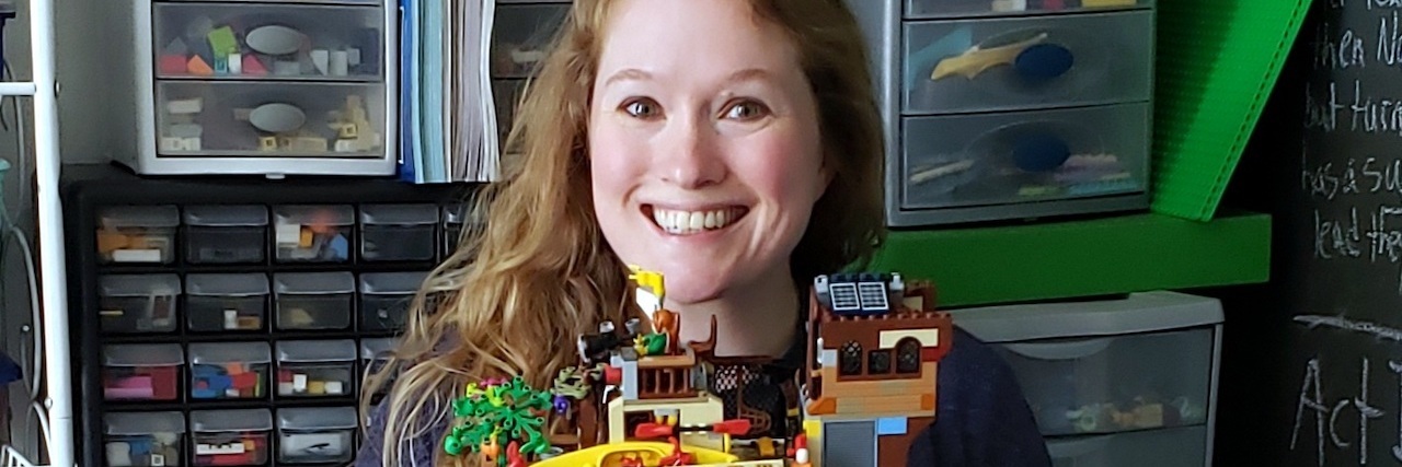 the author holding a Lego boat that she made, smiling