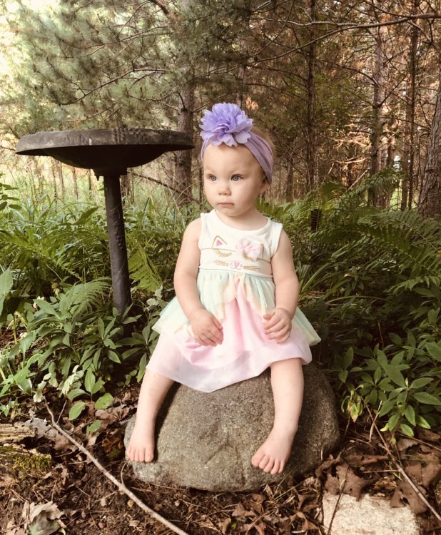 The author's baby sitting on a rock, with a purple bow in her hair