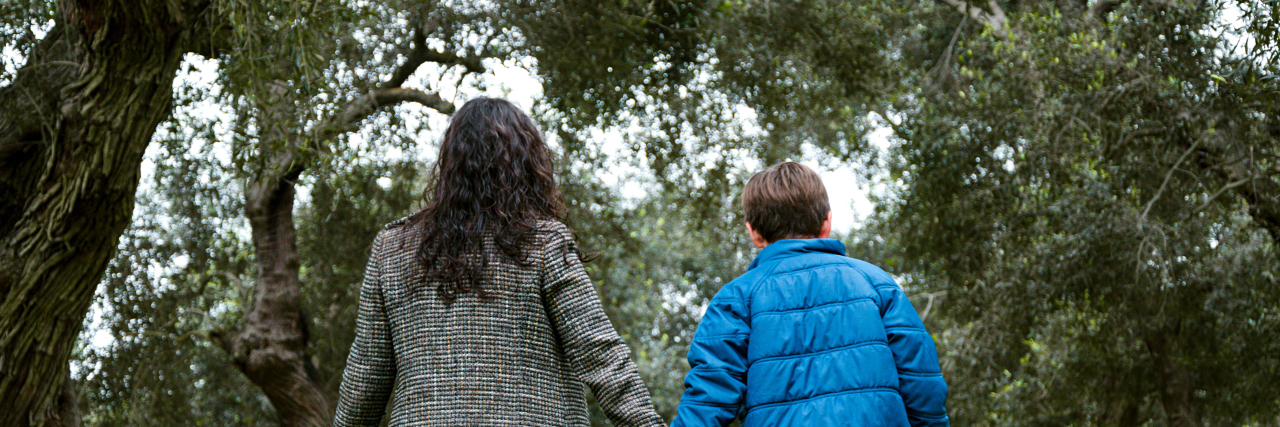 Teaching My Son About Staying Strong in Life With Chronic Illness Mother and son holding hands walking in a park in autumn