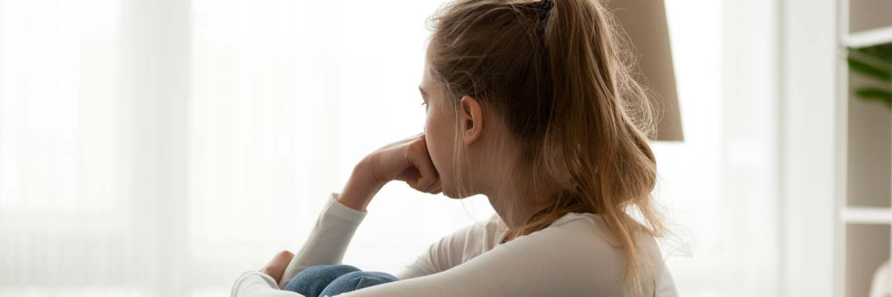 OCD and Perfectionism Stops Me Being Creative photo of young woman sitting on couch looking away from camera toward window, resting chin on her hand