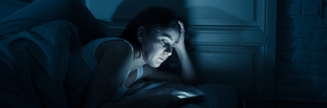 photo of a woman lying in bed at night with her smartphone