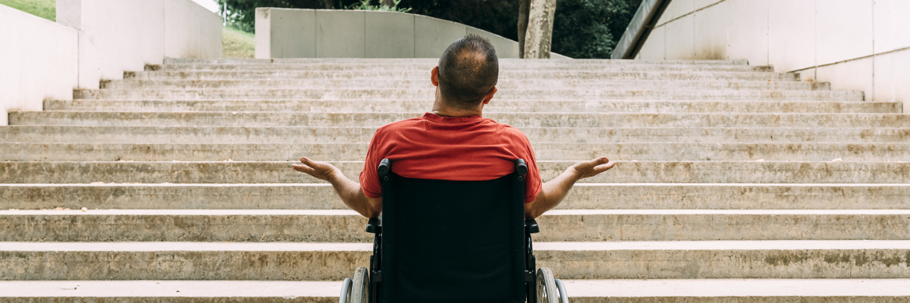 Man in wheelchair outraged in front of stairs.