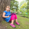Girl with Down syndrome sitting under a tree reading a book.