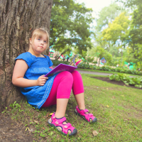 Girl with Down syndrome sitting under a tree reading a book.