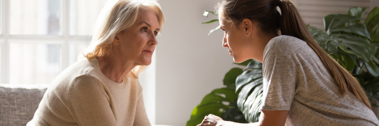 What I Would Tell My Younger Self About Caregiving Adult daughter holding her mother’s hands during an emotional conversation in a bright living room.