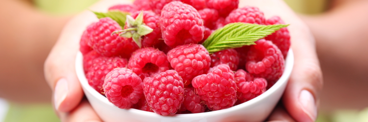 Woman holding a bowl of raspberries.