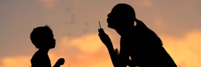 Silhouette of mother and child playing blowing bubbles in the park.