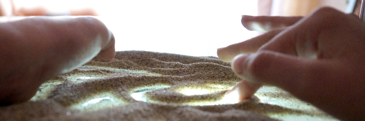 children's hands are engaged in sand therapy on a glass transparent table with backlight
