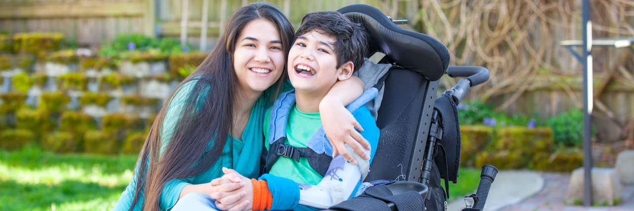 CA Bill Would Reverse Not Offering Unemployment to Caregivers Smiling teenage girl hugging disabled nine year old brother in wheelchair outdoors