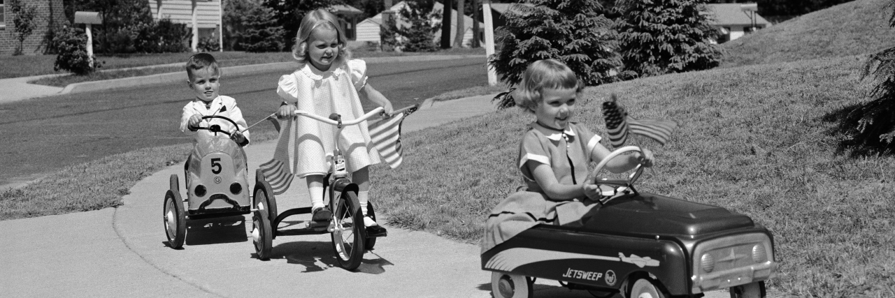 1950s Children on suburban sidewalk, riding tricycle and toy cars.