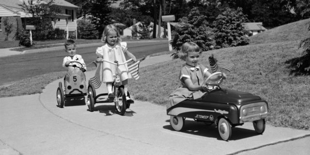 1950s Children on suburban sidewalk, riding tricycle and toy cars.