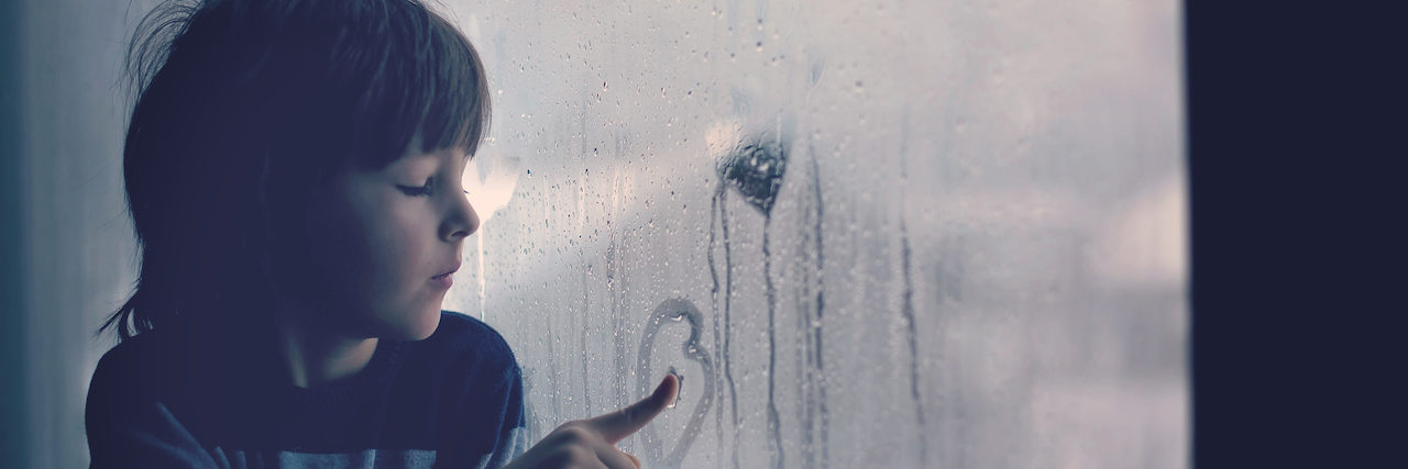 Little boy, leaving finger prints and drawing hearts on a window at home