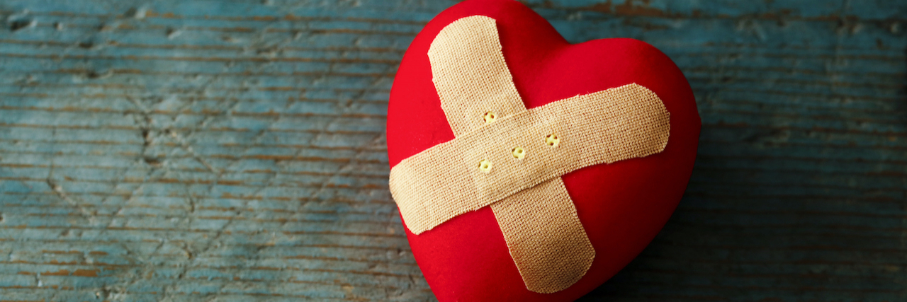 Band-aid covering a heart on a blue wooden background