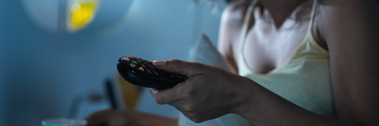 Tips for Watching Shows and Movies That Trigger Your PTSD photo of woman holding a TV remote, zoomed in with serious expression