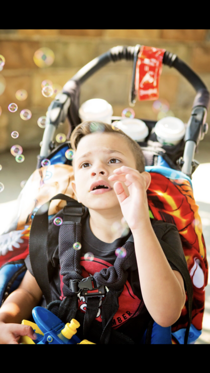 the author's child in a wheelchair/stroller, looking up at bubbles around him, trying to touch them