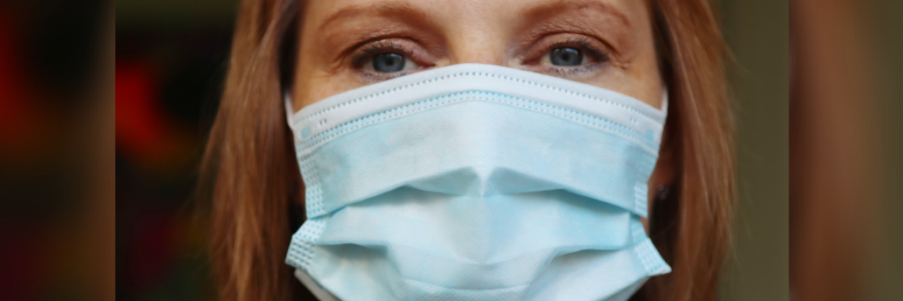 photo of woman wearing a blue medical covid-19 mask looking into camera with serious expression