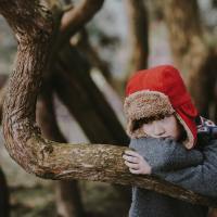 photo of upset looking boy resting his arms and head on a tree branch