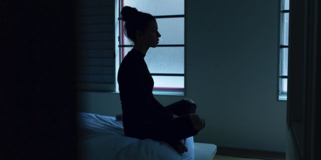 photo of a woman silhouetted against window while sitting on bed in bare room